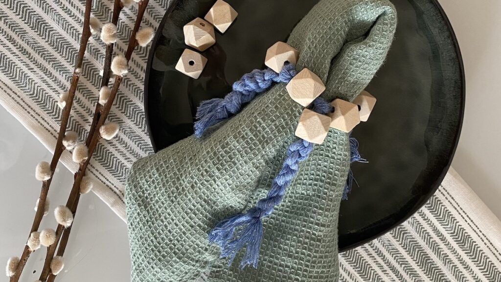 Rond de serviette en perles de bois et macramé bleu sur une serviette en lin vert