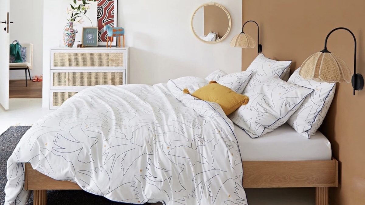 Chambre chaleureuse avec lit en bois, parure de lit blanche à motifs, lampes en rotin et coussin jaune
