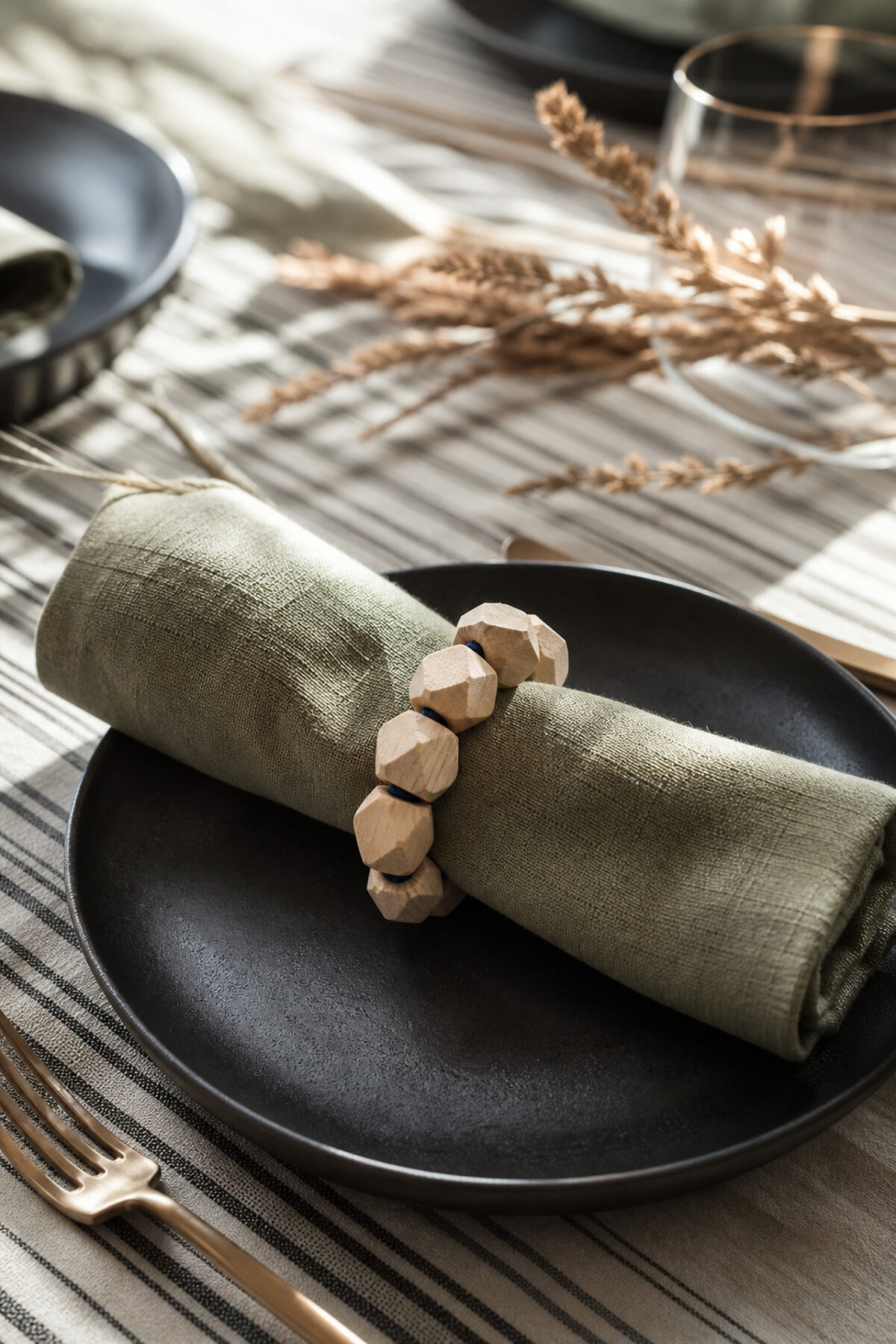 Rond de serviette en perles de bois brut autour d’une serviette en lin vert sur une table élégante