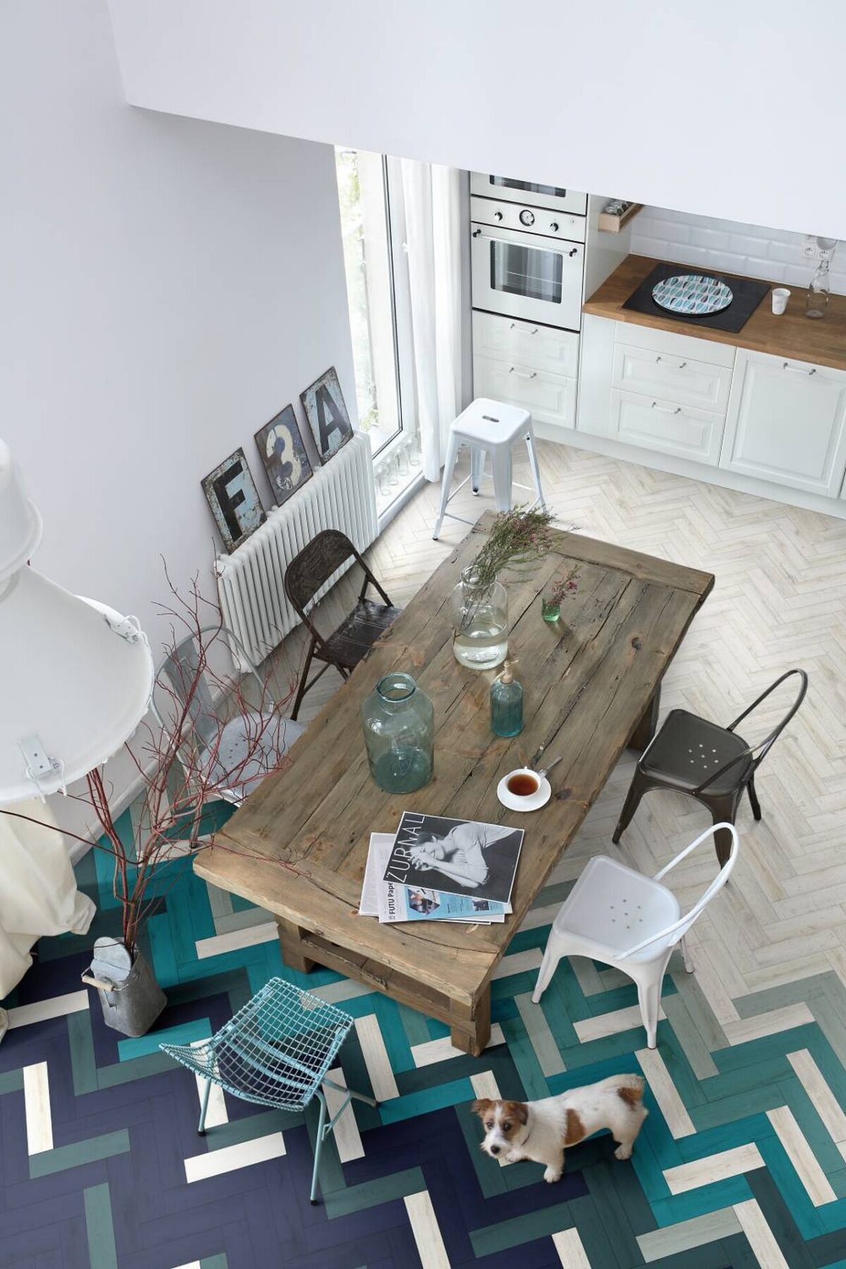 vue en hauteur d’une table en bois avec chaises noires et blanches dépareillées sur un tapis graphique