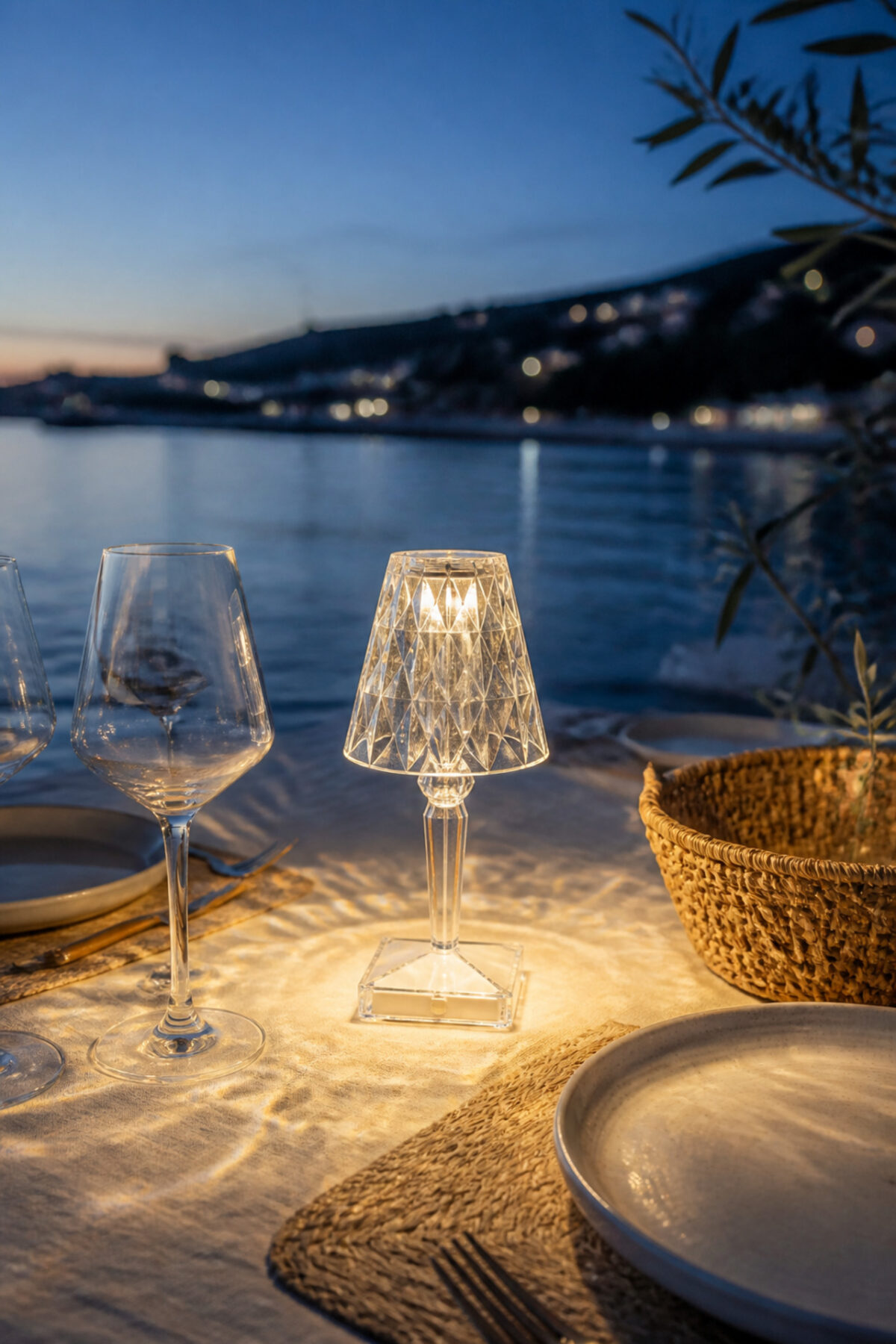 Lampe nomade Battery LED transparente de Kartell posée sur une table de pique-nique au bord de l’eau