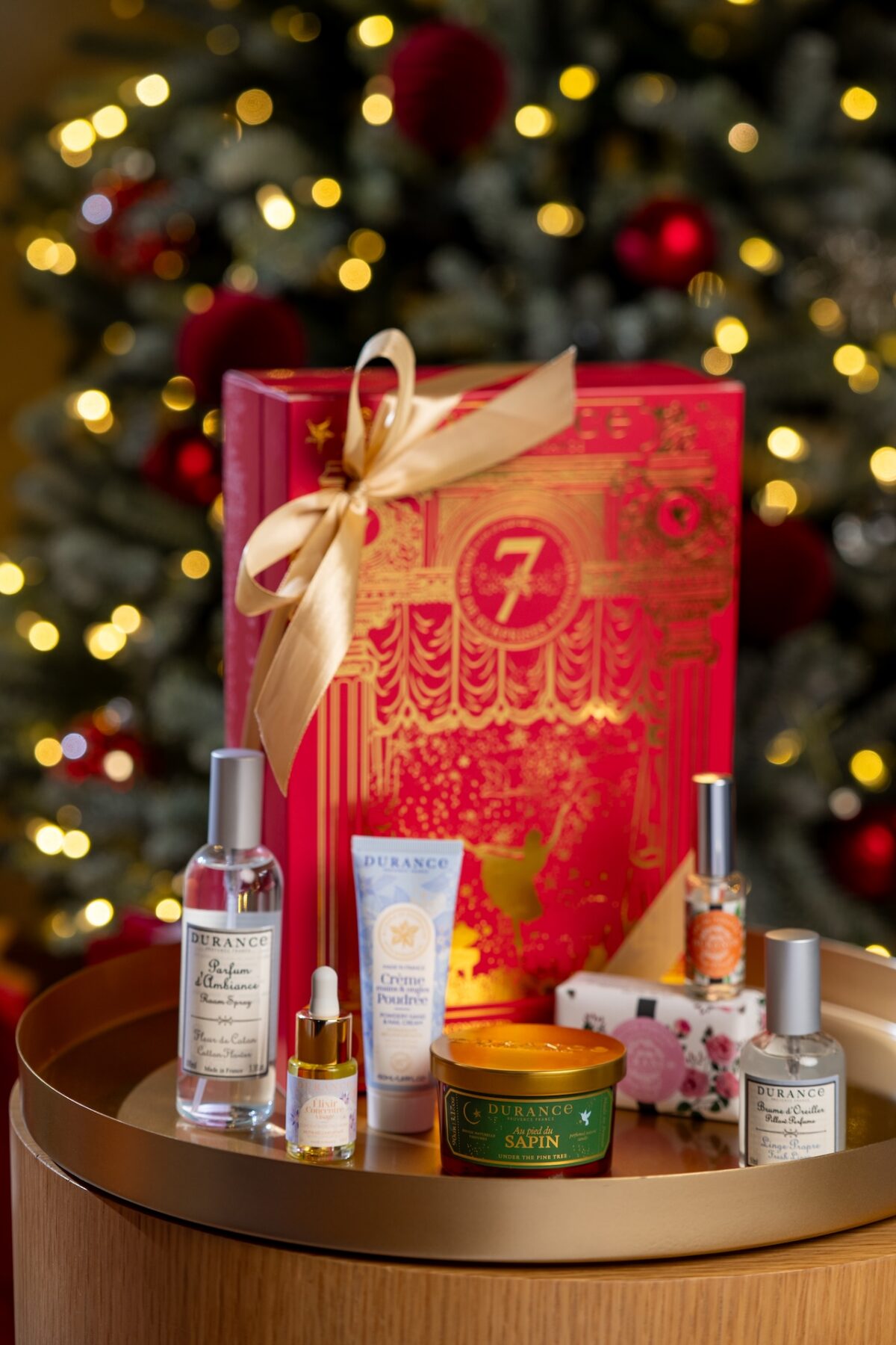 Calendrier de l’Avent Durance rouge et doré posé devant un sapin décoré, entouré de produits parfumés