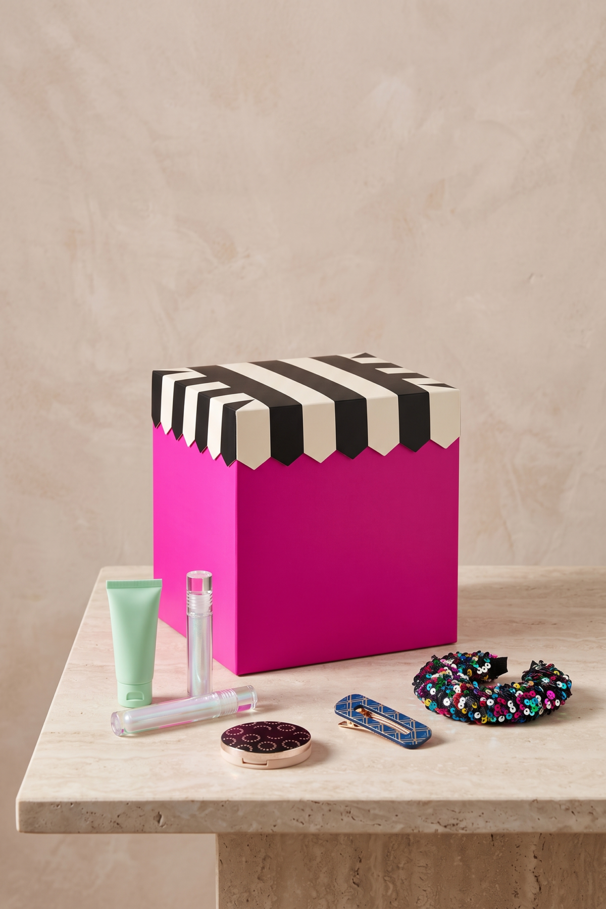 Calendrier de l’Avent Sephora Collection magenta posé avec des accessoires de maquillage colorés.