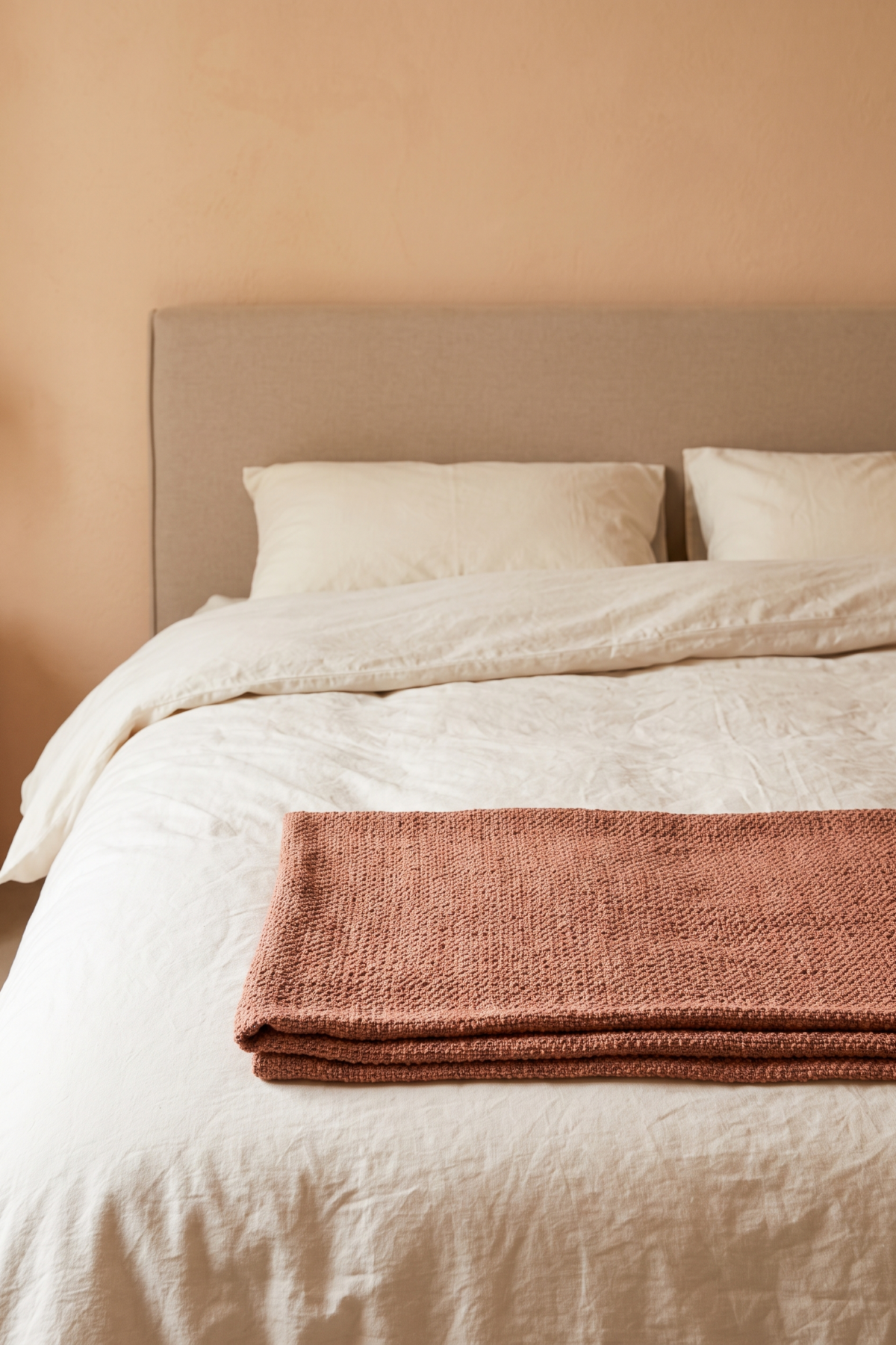 Plaid texturé terracotta plié au pied d’un lit habillé de draps clairs