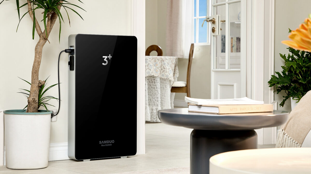 Batterie SAMDUO NEX E6000 noire installée contre un mur clair près d’une plante et d’une porte vitrée dans un salon