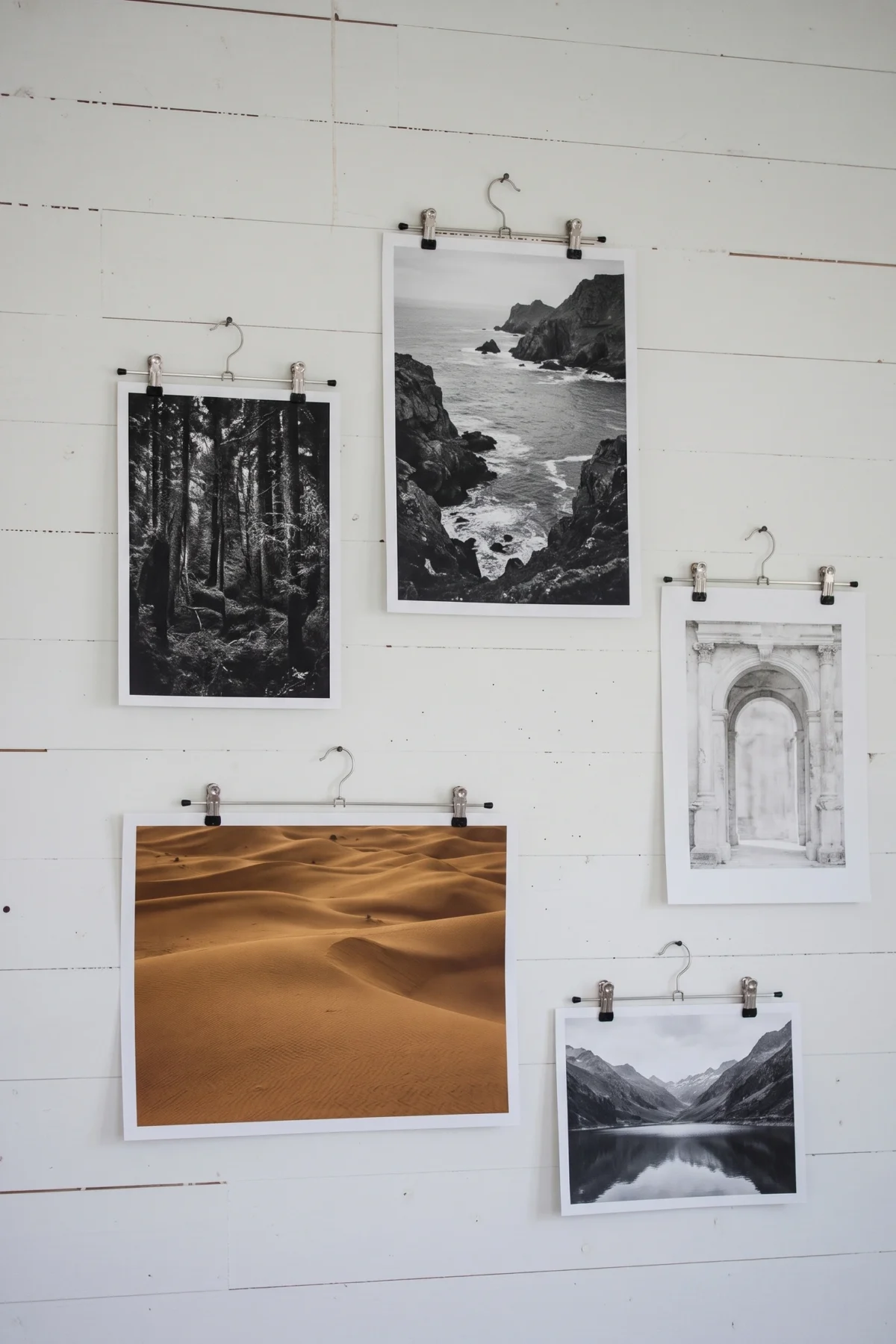 Photographies de paysages suspendues à des cintres métalliques sur un mur blanc