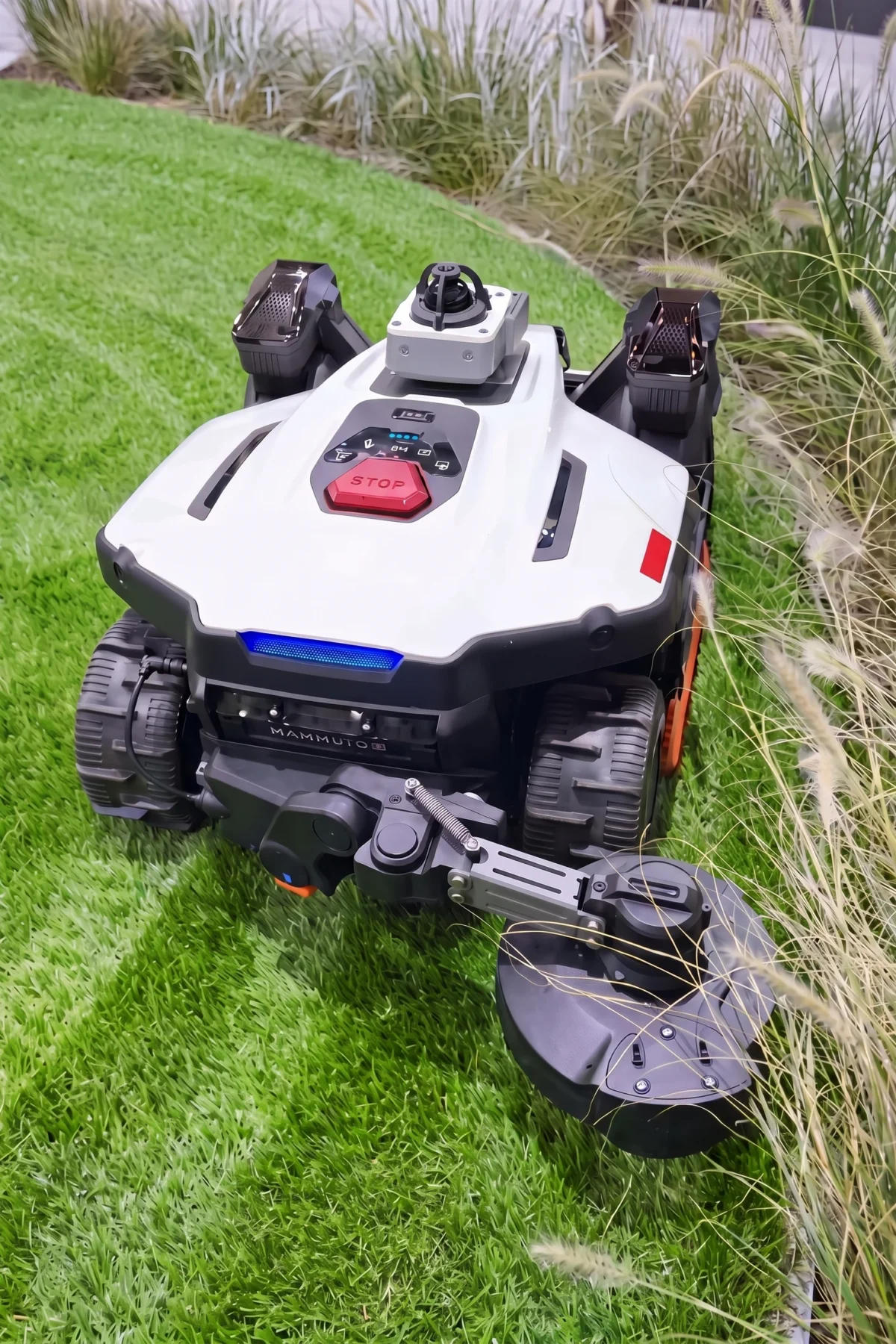Robot tondeuse blanc et noir avec bras coupe-bordures déployé au bord d’une pelouse